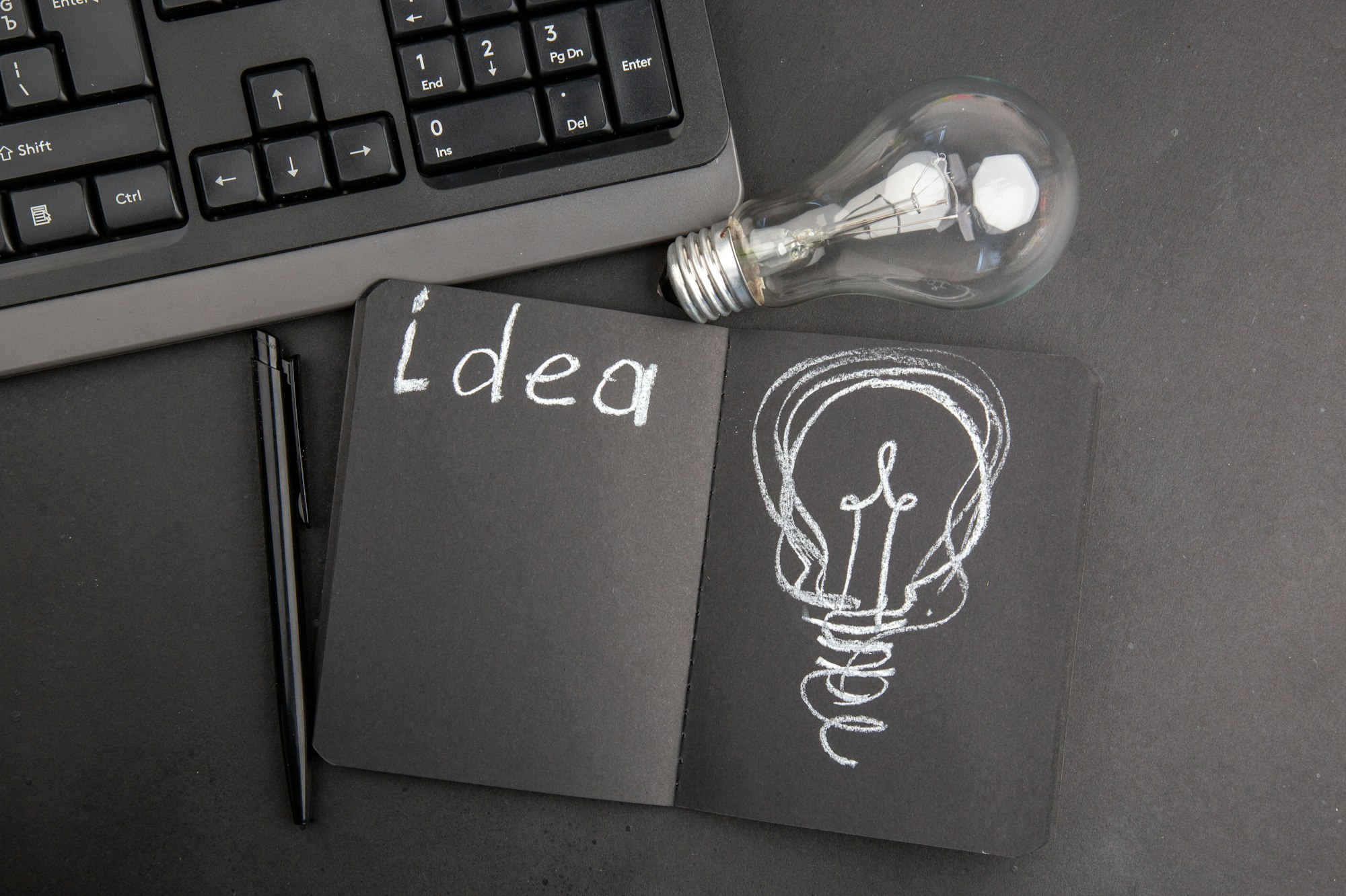 top view idea light bulb drawing on notepad keyboard pen light bulb on dark background